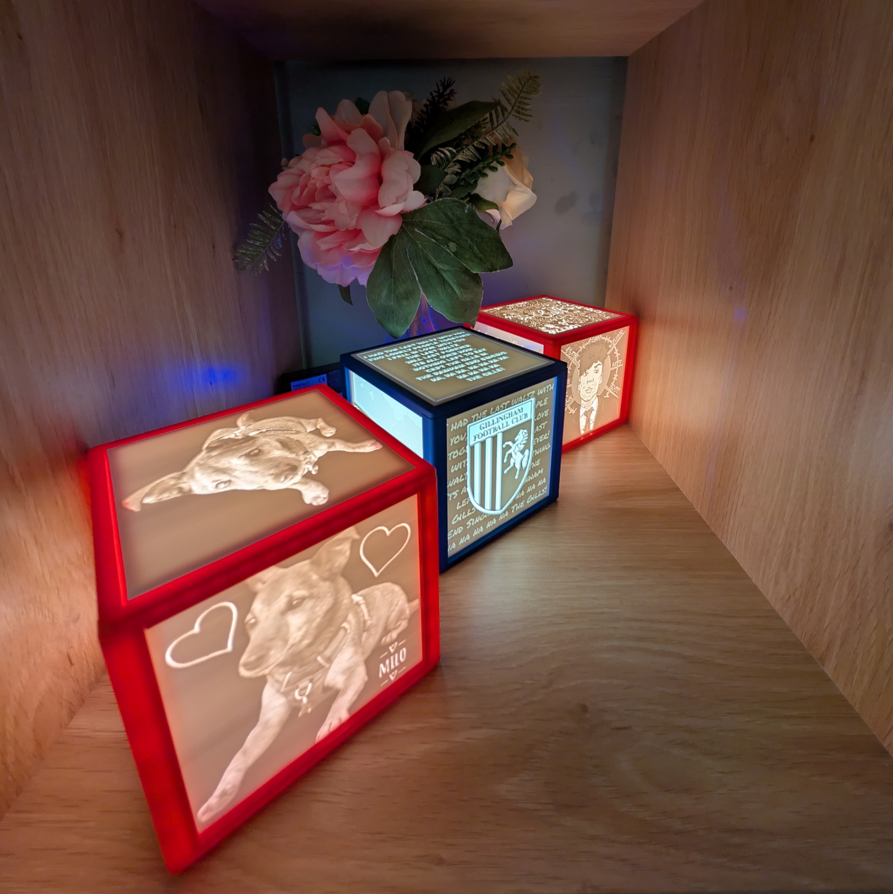 Three lithophane light boxes with red, blue and pink frames glowing on a shelf